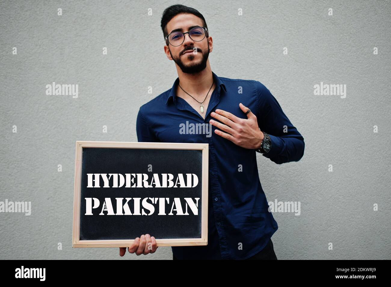 Uomo arabo indossare camicia blu e occhiali tenere tavola con l'iscrizione Hyderabad Pakistan. Le città più grandi del mondo islamico concetto. Foto Stock