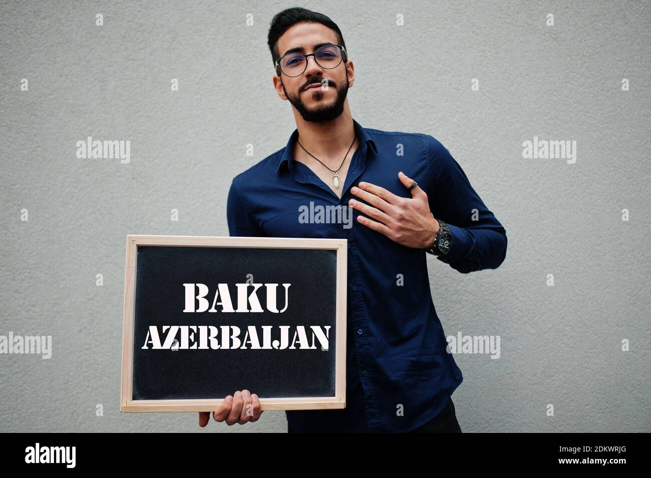 Uomo arabo indossare camicia blu e occhiali tenere tavola con l'iscrizione Baku Azerbaigian. Le città più grandi del mondo islamico concetto. Foto Stock