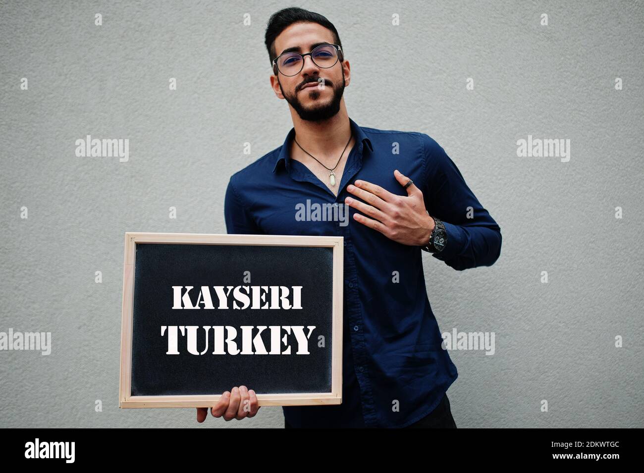 Uomo arabo indossare camicia blu e occhiali tenere tavola con l'iscrizione Kayseri Turchia. Le città più grandi del mondo islamico concetto. Foto Stock