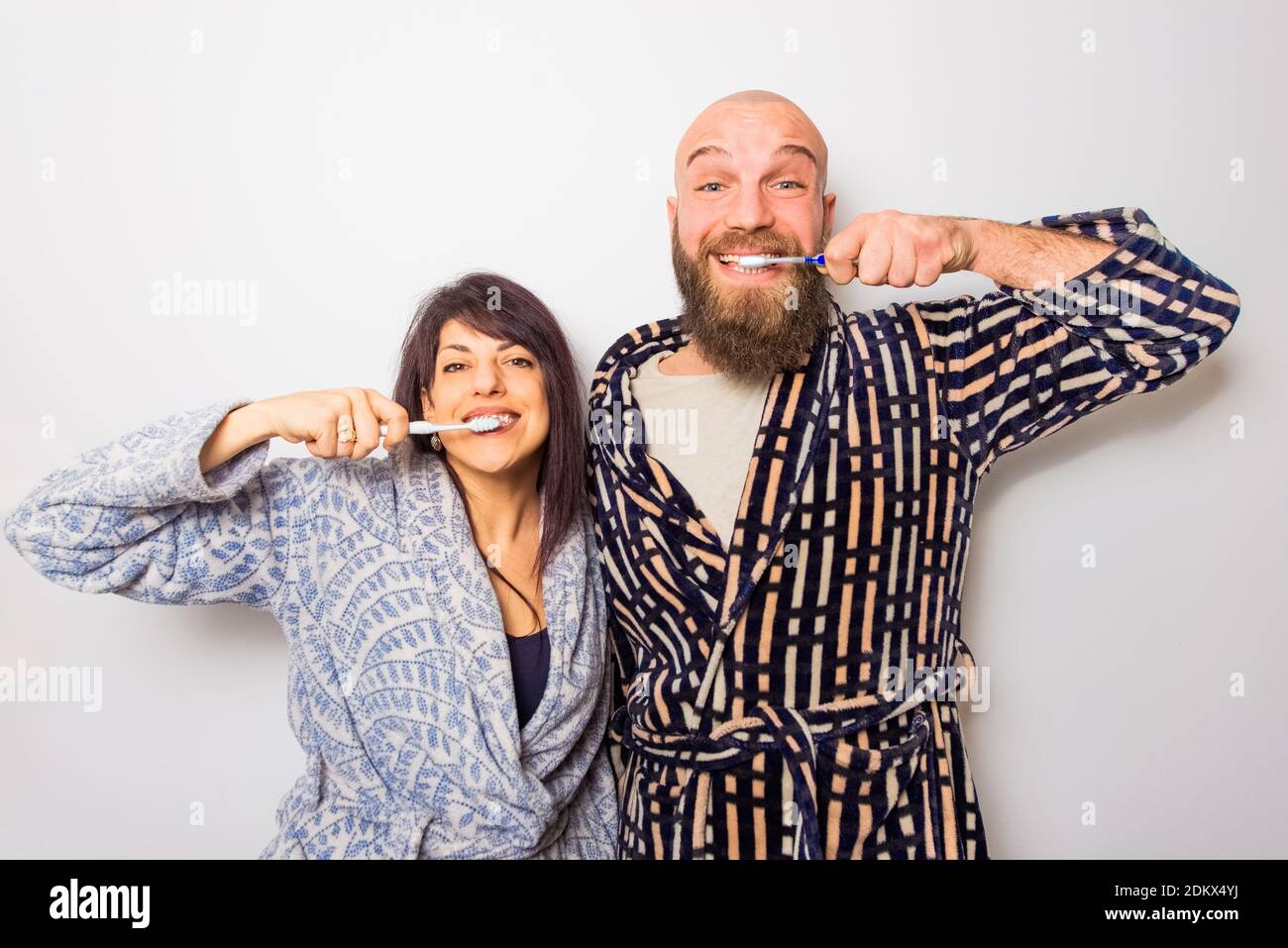 coppia felice di un uomo calvo di hipster e una donna di brunetta caucasica usando uno spazzolino da denti simultaneamente isolato su uno sfondo bianco.buon umore del mattino. Foto Stock