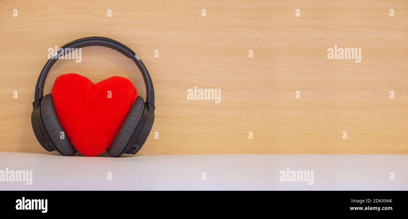 San Valentino 2021. Ascolto a cuore rosso con auricolare su tavola di legno. Giorno degli amanti. Foto Stock