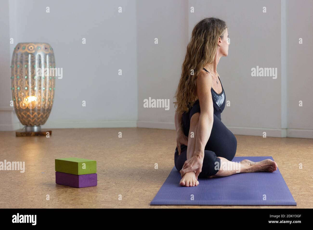 Donna di mezza età in ardha matsyendrasana asana in studio. Yoga avanzato praticante in mezzo signore dei pesci posa con i puntelli sul lato Foto Stock