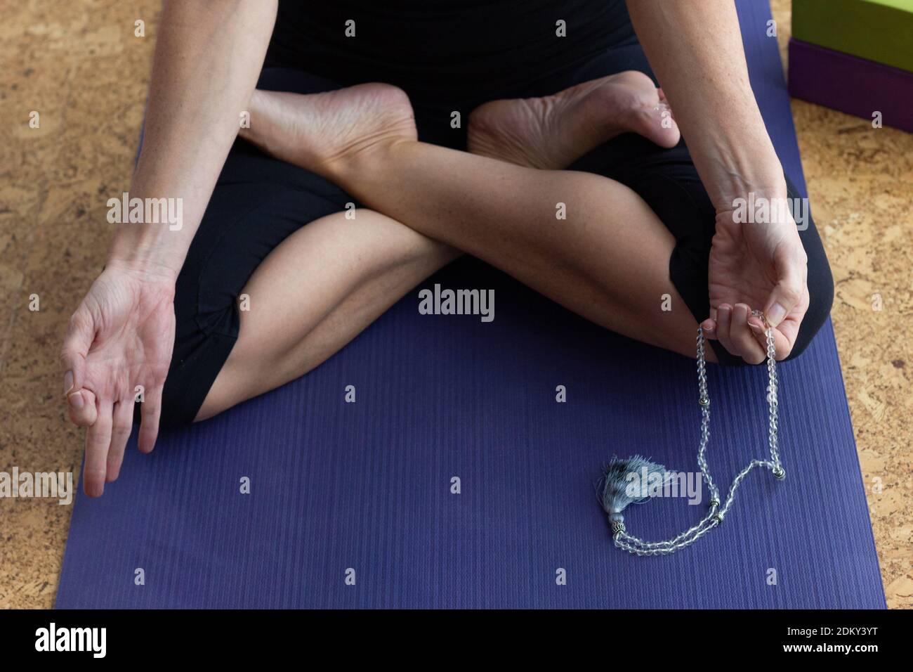 Donna anonima seduta in posa di loto sul tappeto di yoga tiene perline di mala per il conteggio dei mantra. Yoga femminile che pratica la meditazione rituale di formazione. Concetto Zen Foto Stock