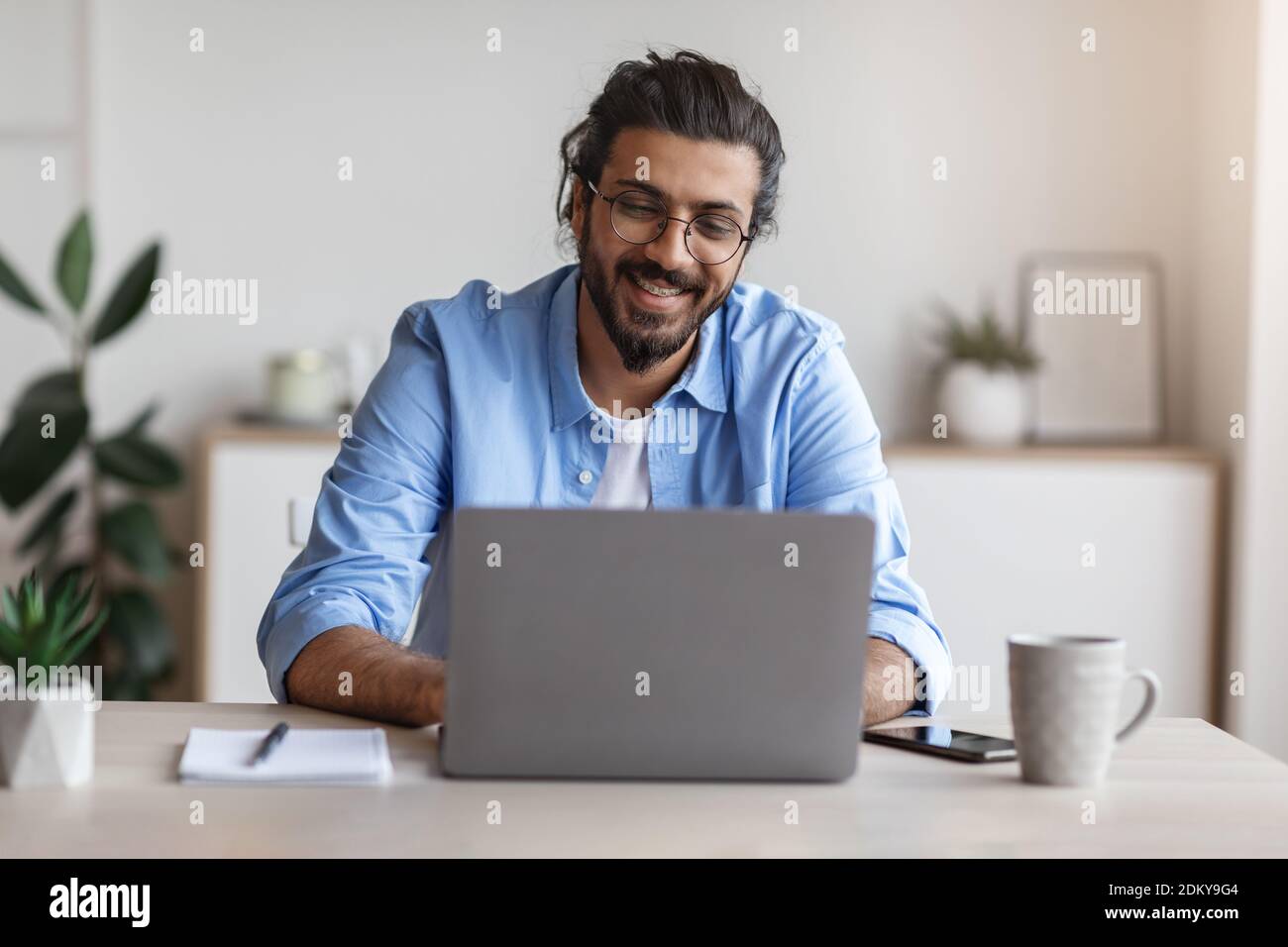 Lavoro freelance. Happy Millennial Arab Man lavorando al computer presso l'ufficio di casa Foto Stock