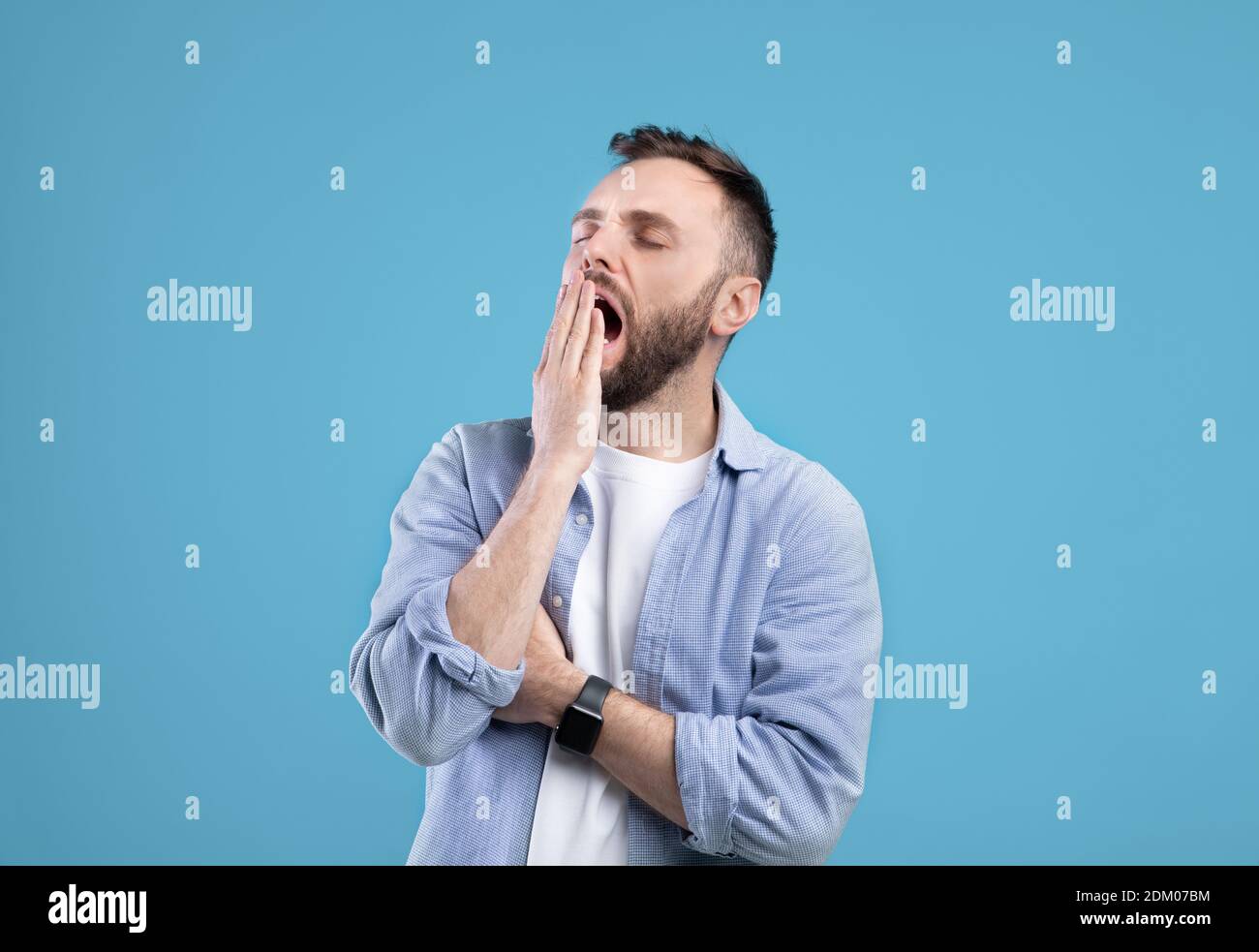 Annoiato giovane ragazzo yawning, che copre bocca aperta con mano su sfondo blu studio Foto Stock