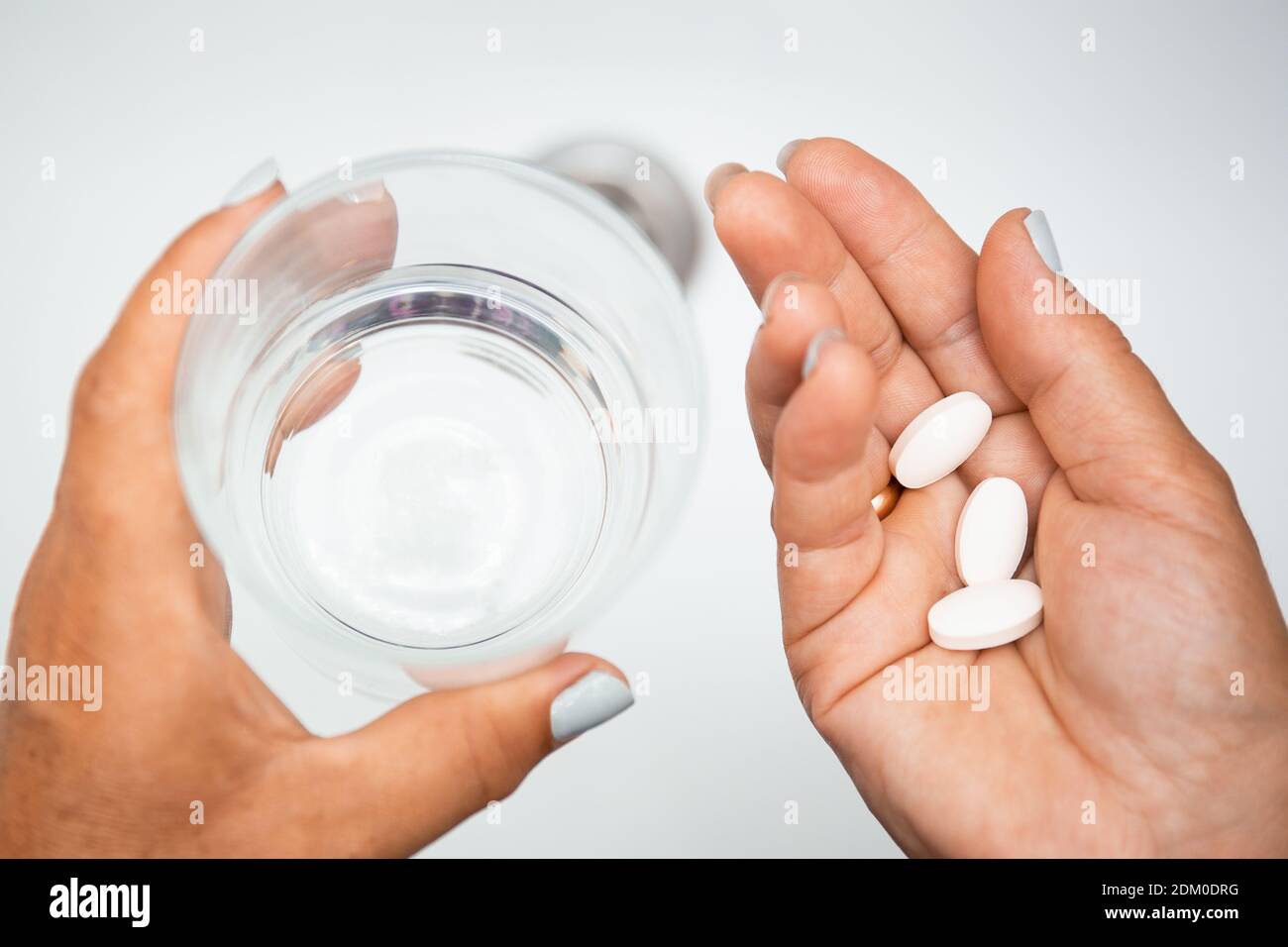 Donna anziana mano con pillole compresse di medicina e un bicchiere d'acqua contro lavelli bianchi con acqua dolce. Donna anziana che prende le pillole a casa, closeup. D Foto Stock