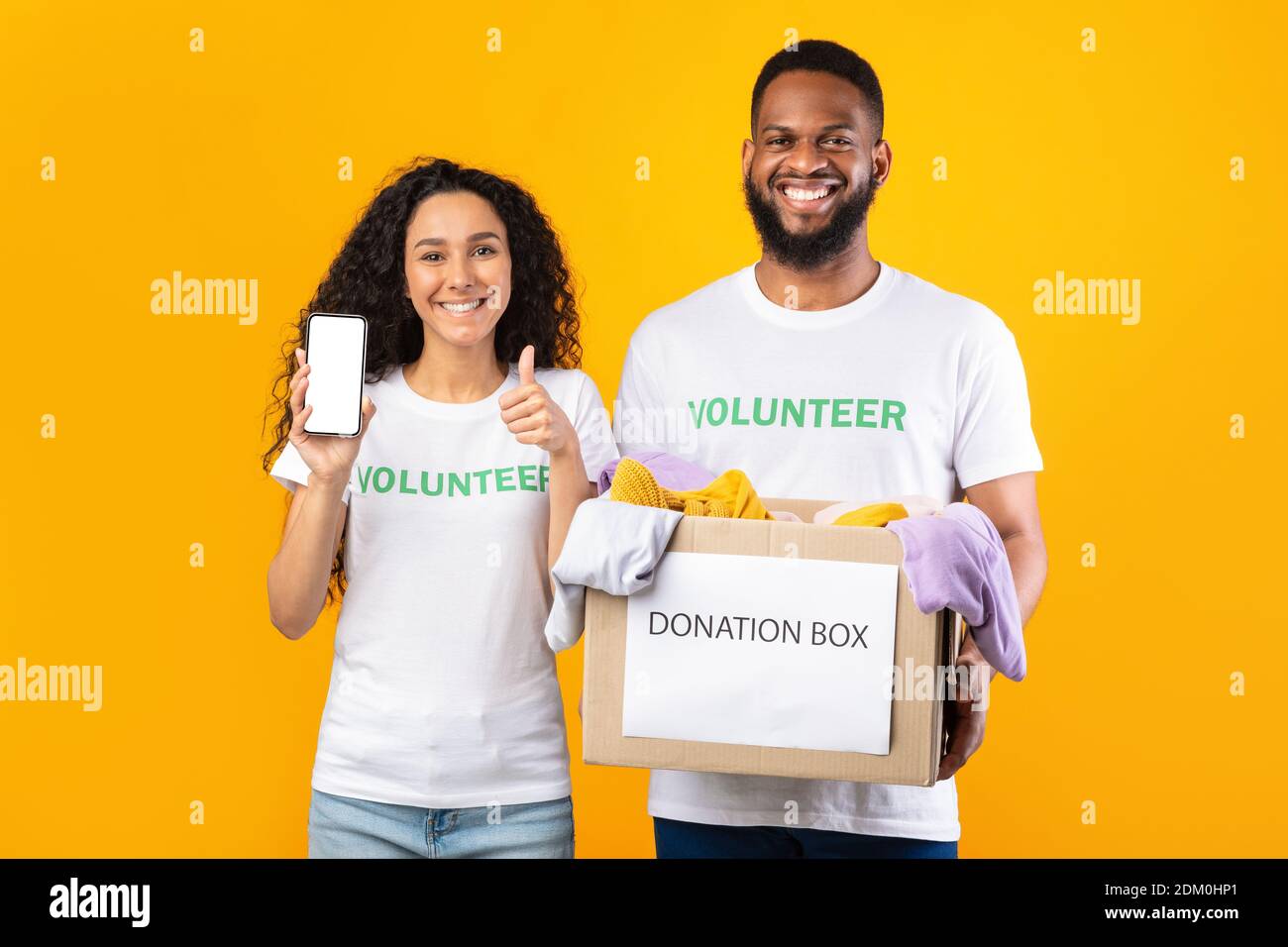 Due Volontarii che Holding Donation Box che mostra la schermata Telefono, sfondo giallo Foto Stock