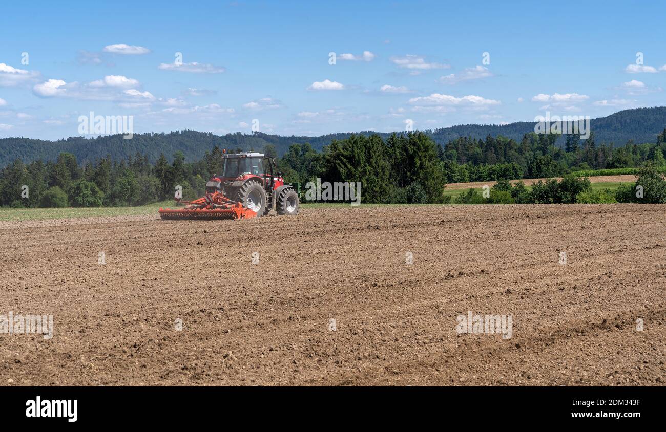 Trattore mentre si erala la terra marrone in un campo Foto Stock