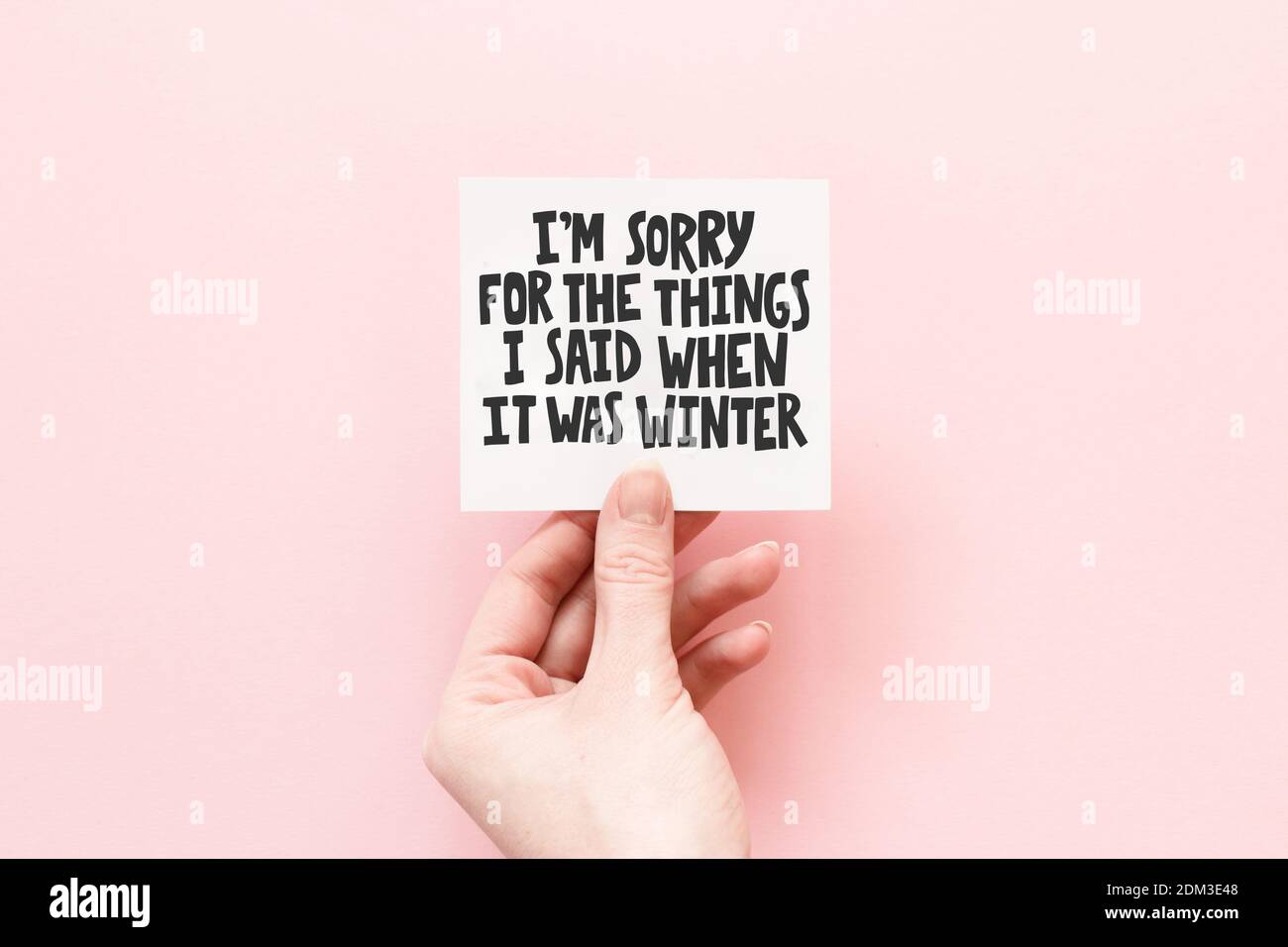 Composizione minima su sfondo rosa pastello con la mano della ragazza Tenendo carta con citazione mi dispiace per le cose che ho ha detto quando era inverno Foto Stock