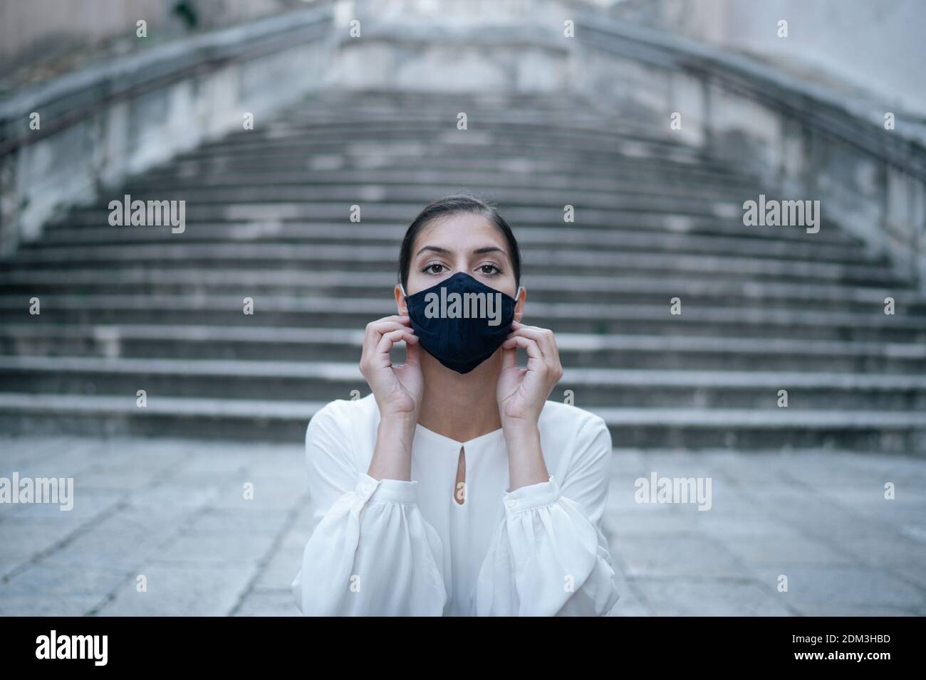 Donna depressa preoccupata che indossa una maschera di tessuto riutilizzabile durante il coronavirus COVID-19 focolaio.ritratto emotivo della persona interessata in una strada vuota. Foto Stock