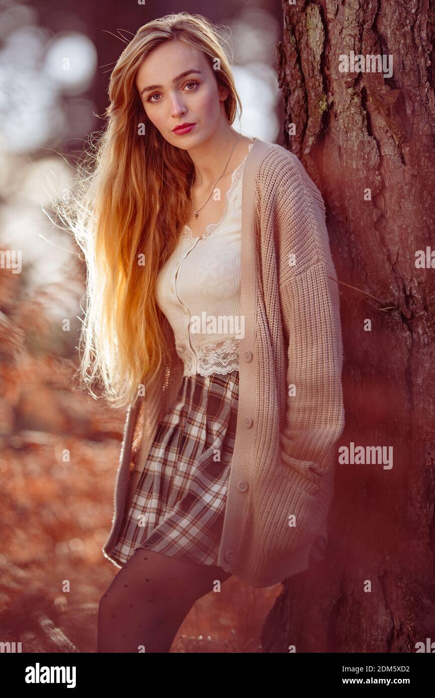 Una giovane donna (20 anni) di bellezza naturale con lunghi capelli biondi si pone in una foresta Autumnal di tonalità arancio in un sole giorno di dicembre. Foto Stock