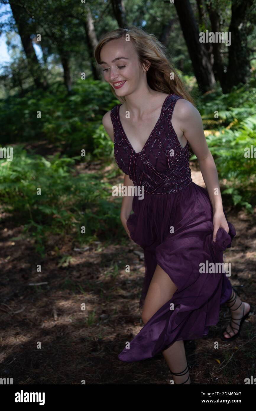 Una giovane donna naturalmente bella con lunghi capelli biondi vestita in un abito viola palla corre e twirls divertirsi in un ambiente di campagna. Foto Stock