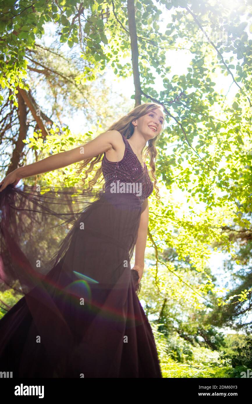 Una giovane donna naturalmente bella con lunghi capelli biondi vestita in un abito viola palla corre e twirls divertirsi in un ambiente di campagna. Foto Stock