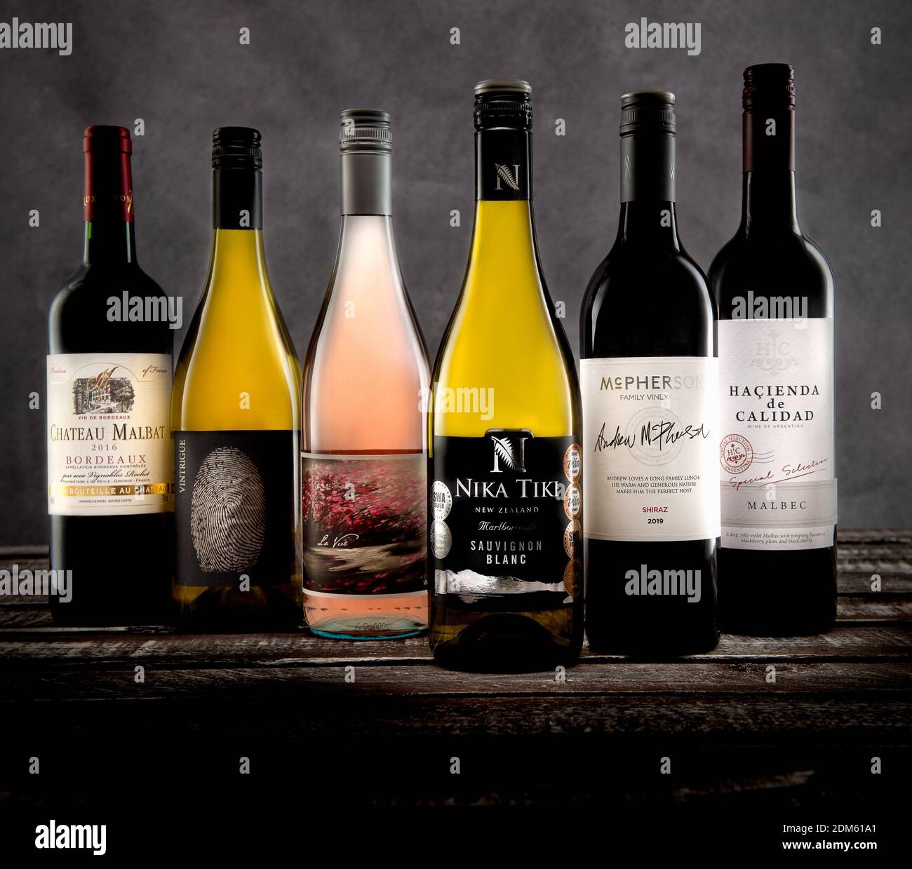 Un mix di sei bottiglie di vino rosso e bianco sparate nello studio su uno sfondo grigio in tela e su una base in legno. Foto Stock