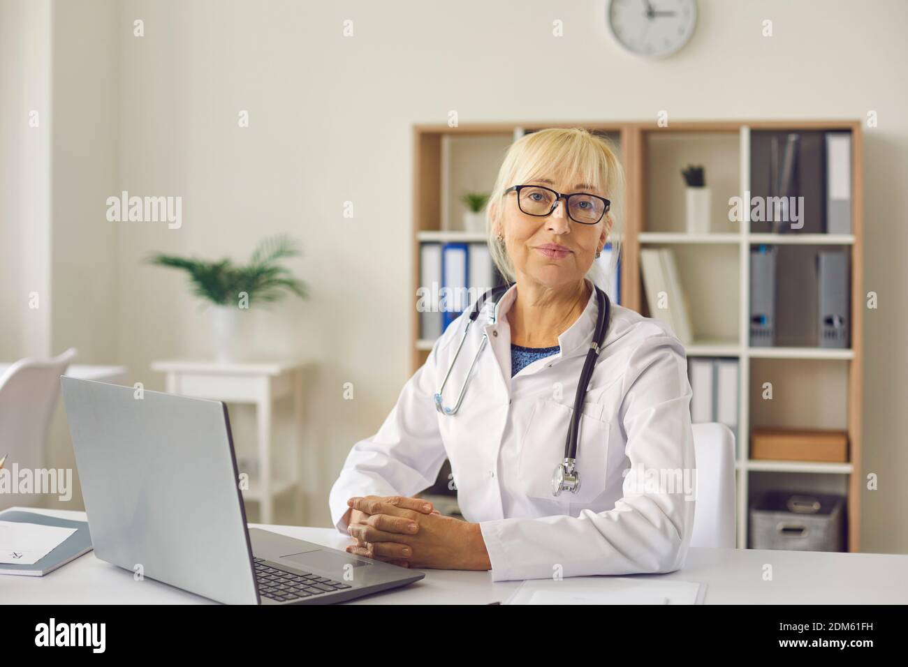Ritratto di medico esperto seduto alla scrivania con il computer portatile sul suo posto di lavoro Foto Stock
