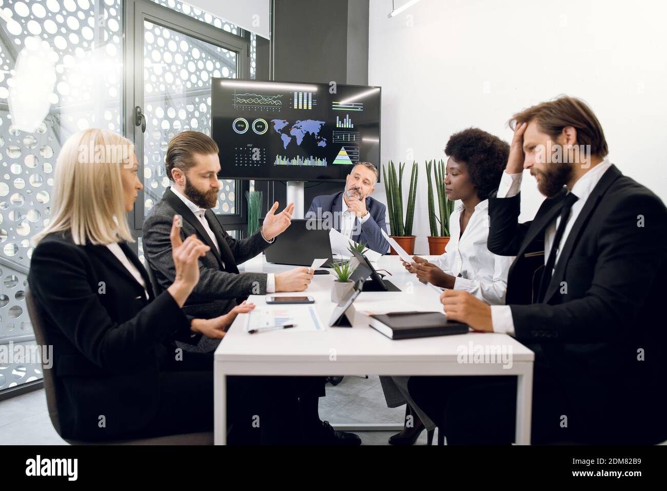 Economisti o direttori multietnici, uomini e donne sicuri, che discutono della strategia aziendale durante il brainstorming in ufficio, con la mappa mondiale e. Foto Stock