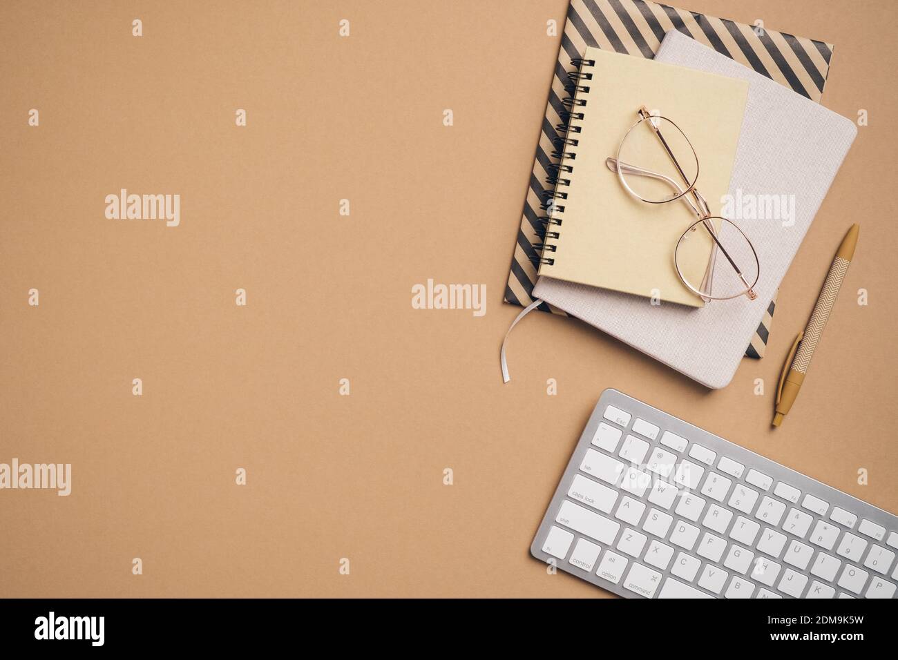 Scrivania moderna vista dall'alto con notebook in carta, tastiera, forniture per ufficio, occhiali su sfondo beige. Disposizione piatta. Concetto aziendale. Foto Stock