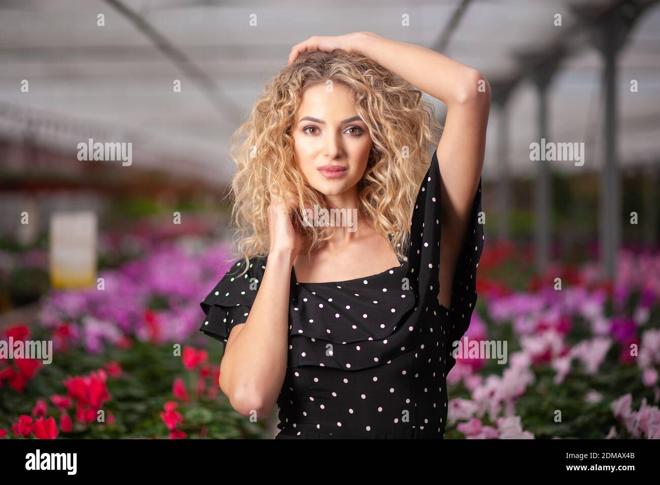 giovane bella ragazza si leva in piedi in un arrangiamento di fiori tra i fiori e guarda nella fotocamera Foto Stock