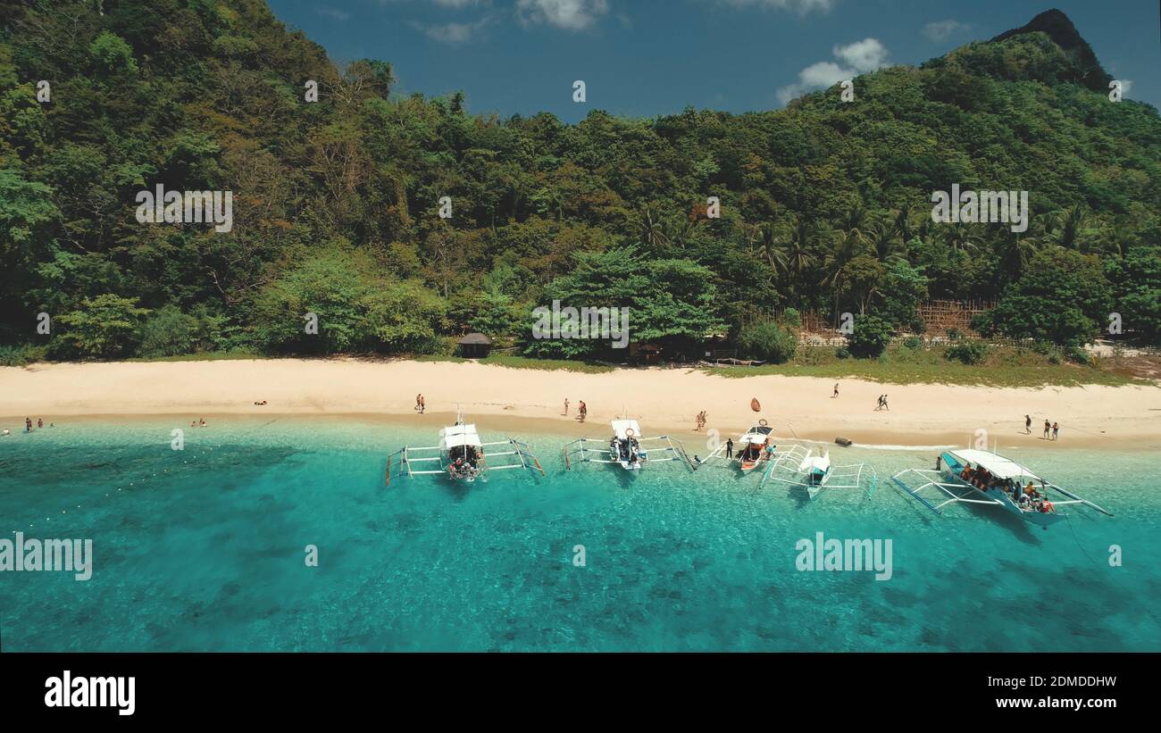 Crociera tropicale con persone che riposano in aereo sulla riva dell'oceano. Porto epico con le barche da passeggeri tradizionali sulla spiaggia di sabbia delle isole El Nido, Palawan, Filippine, Asia. Verde paesaggio boschivo di monte Foto Stock