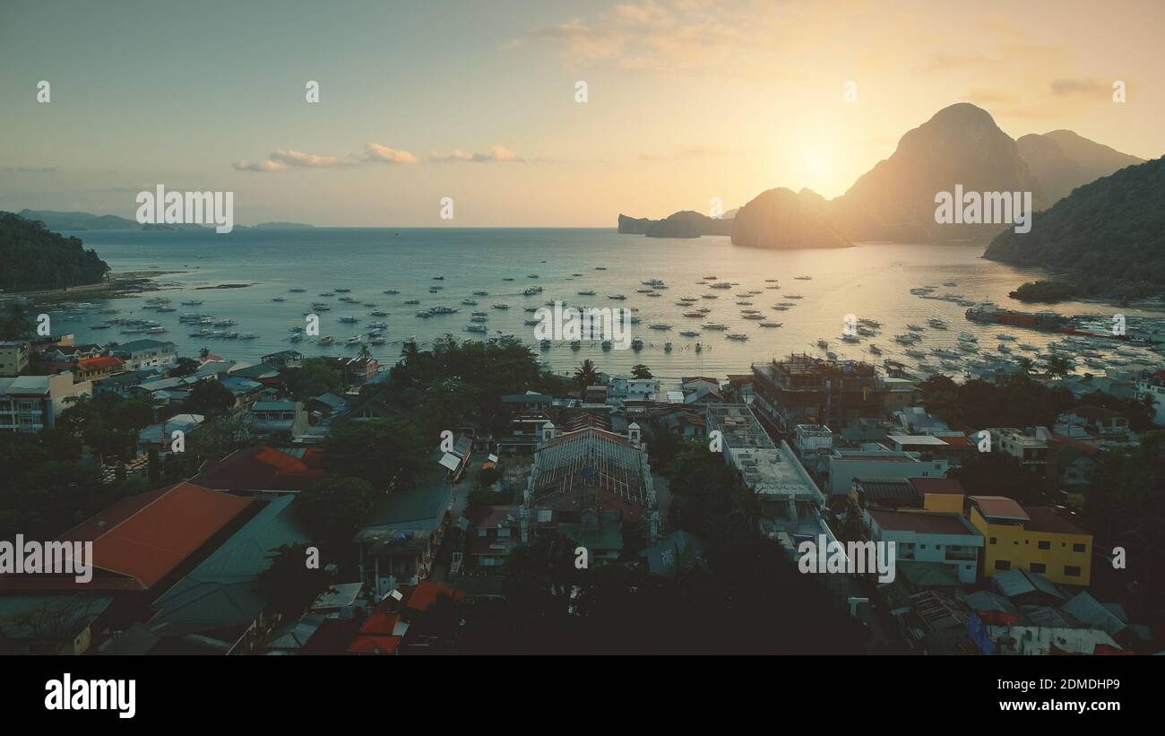 Vista aerea della baia dell'oceano del tramonto al porto con trasporto d'acqua in un paesaggio urbano tropicale. Città paradisiaca delle isole Filippine. Monte verde con alberi di bosco in estate soleggiato giorno. Scatto con drone cinematografico Foto Stock