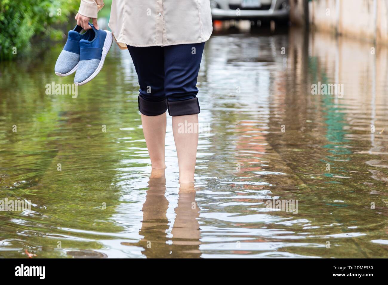 Donna che cammina su strada allagata con scarpe di tenuta dopo il piogge  pesanti, causa di prurito della pelle includono, fare attenzione alla  leptospirosi, può essere infettati dal contatto con l'acqua, il