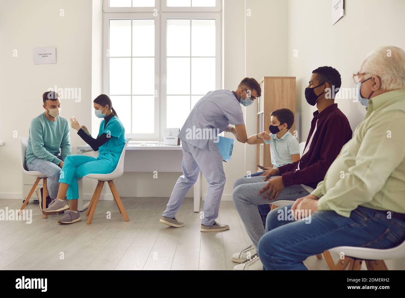 Persone diverse in maschere mediche di fronte seduti in linea, in attesa di ottenere l'influenza o Covid-19 vaccino Foto Stock