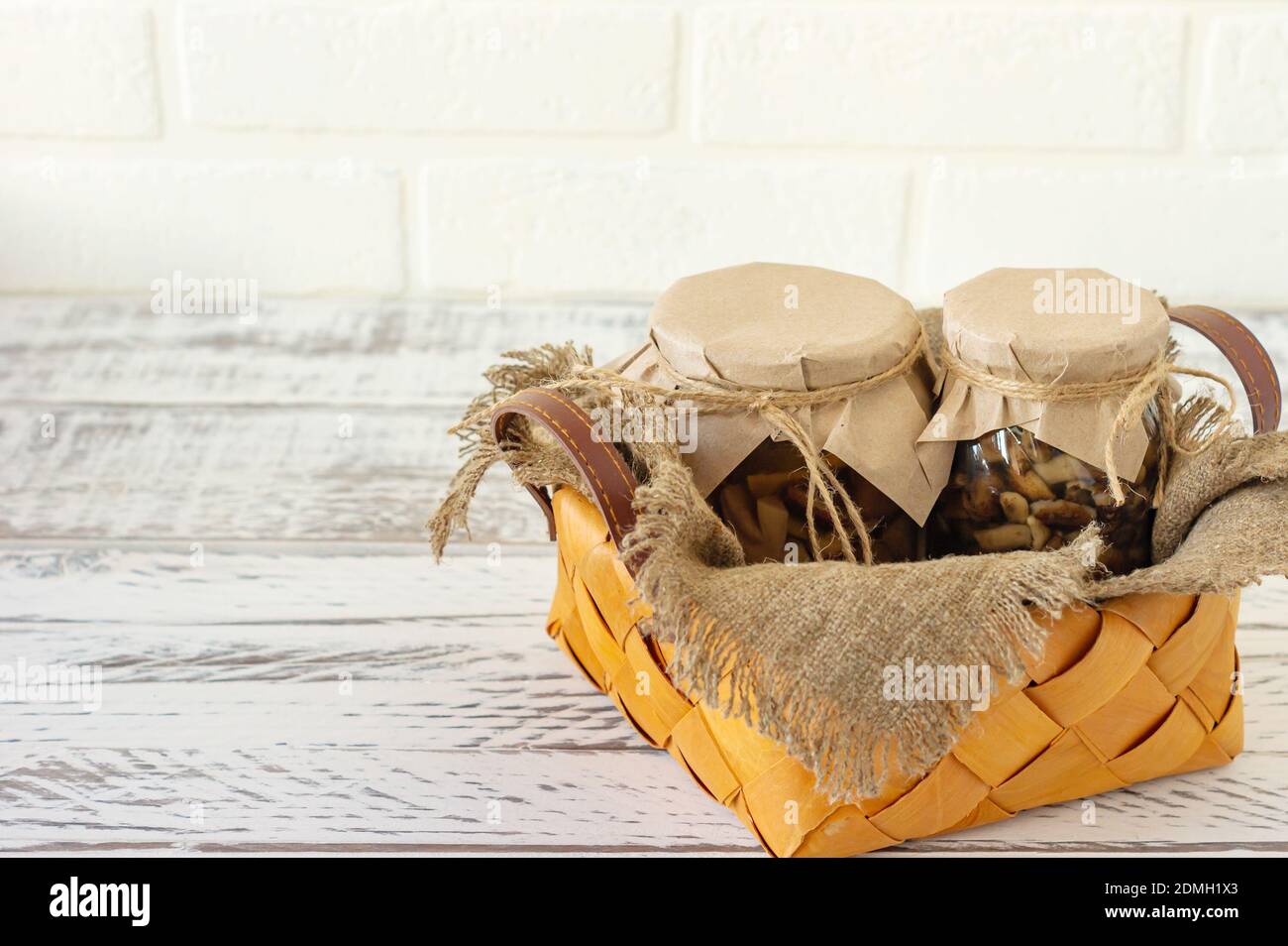 Vasetti di vetro con funghi in scatola in un cestino. Cibo fermentato su sfondo bianco con spazio di copia. Foto Stock