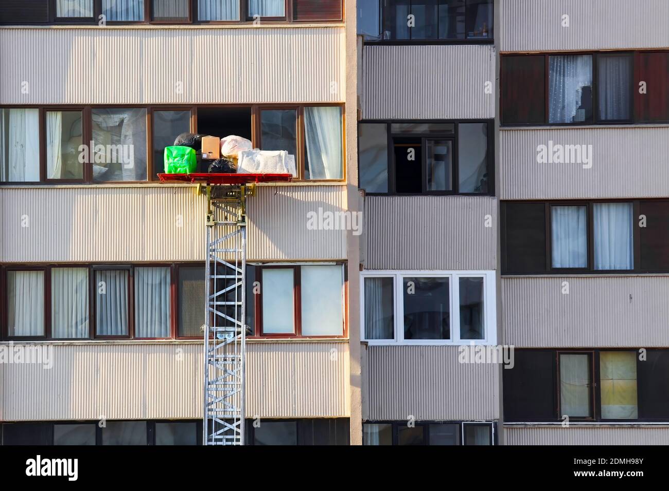 Smontaggio dell'alloggiamento con una scaletta idraulica o un sollevatore. Trasportatori che trasportano o raccolgono mobili utilizzando un ascensore meccanico attraverso la finestra di un'edilina urbana Foto Stock