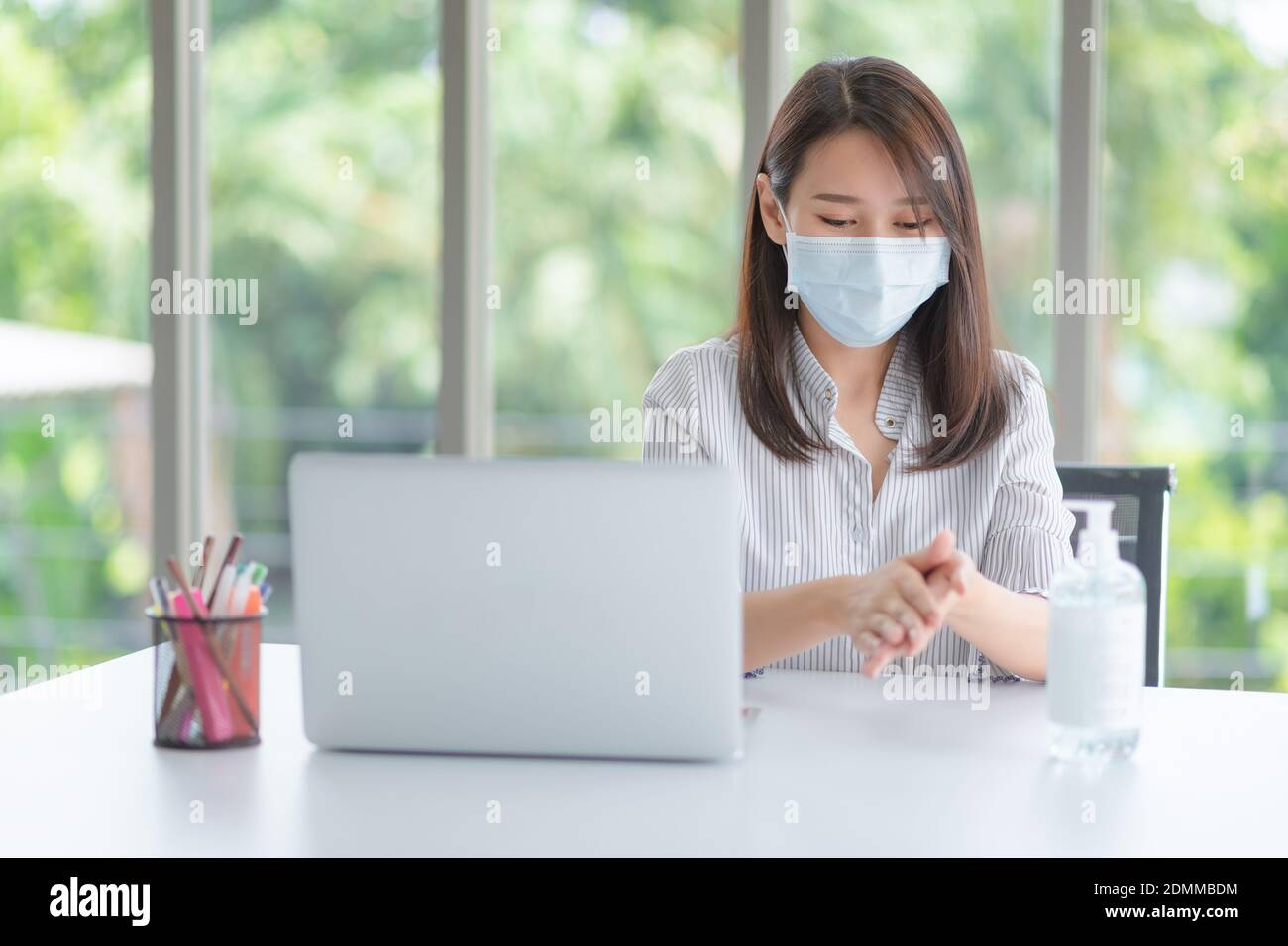 Donna d'affari che indossa la maschera e usa l'igienizzatore personale per la pulizia La sua mano in ufficio per mantenere l'igiene.preventiva durante il periodo di epidemia da Foto Stock