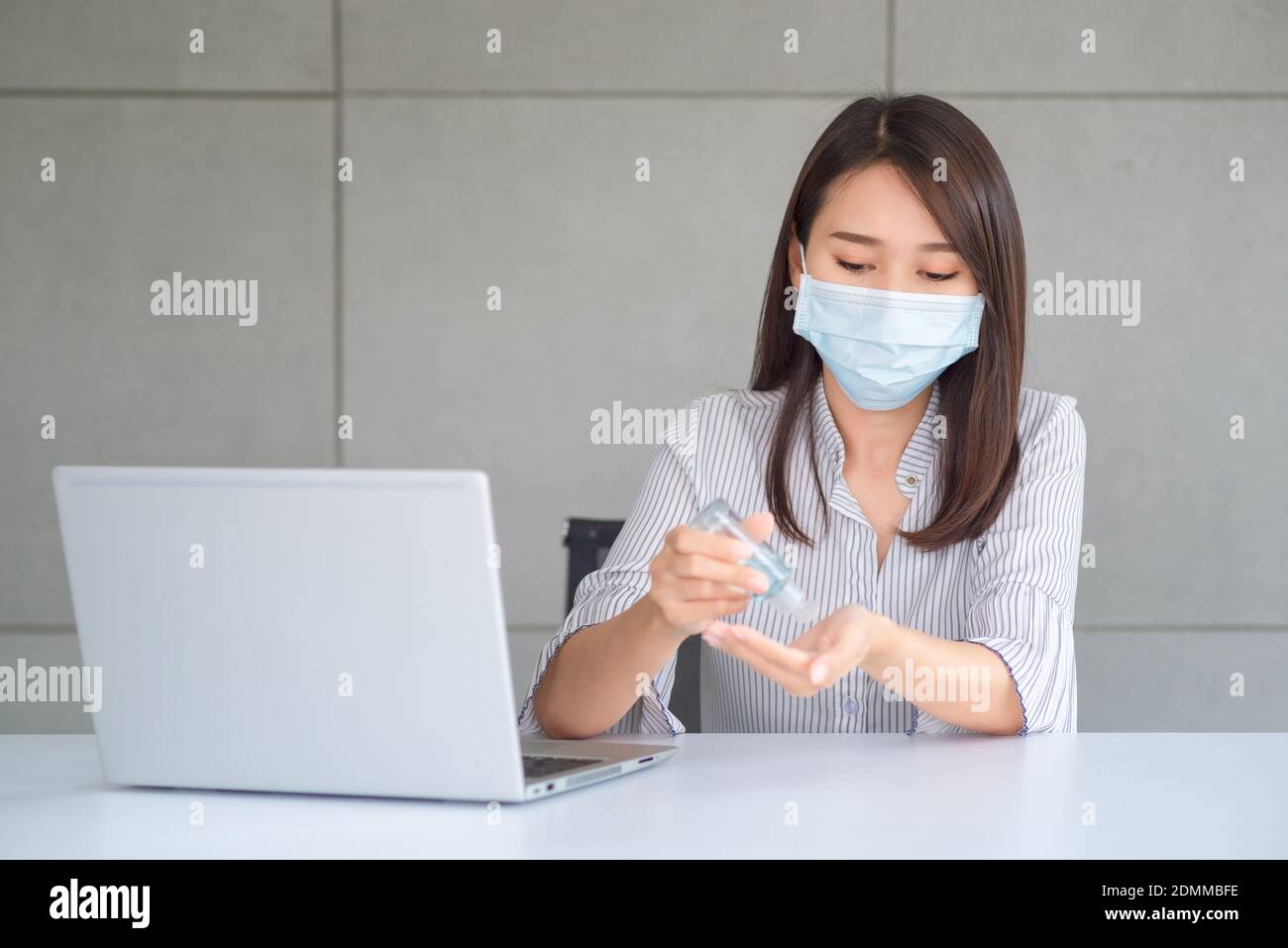 Donna d'affari che indossa la maschera e usa l'igienizzatore personale per la pulizia La sua mano in ufficio per mantenere l'igiene.preventiva durante il periodo di epidemia da Foto Stock