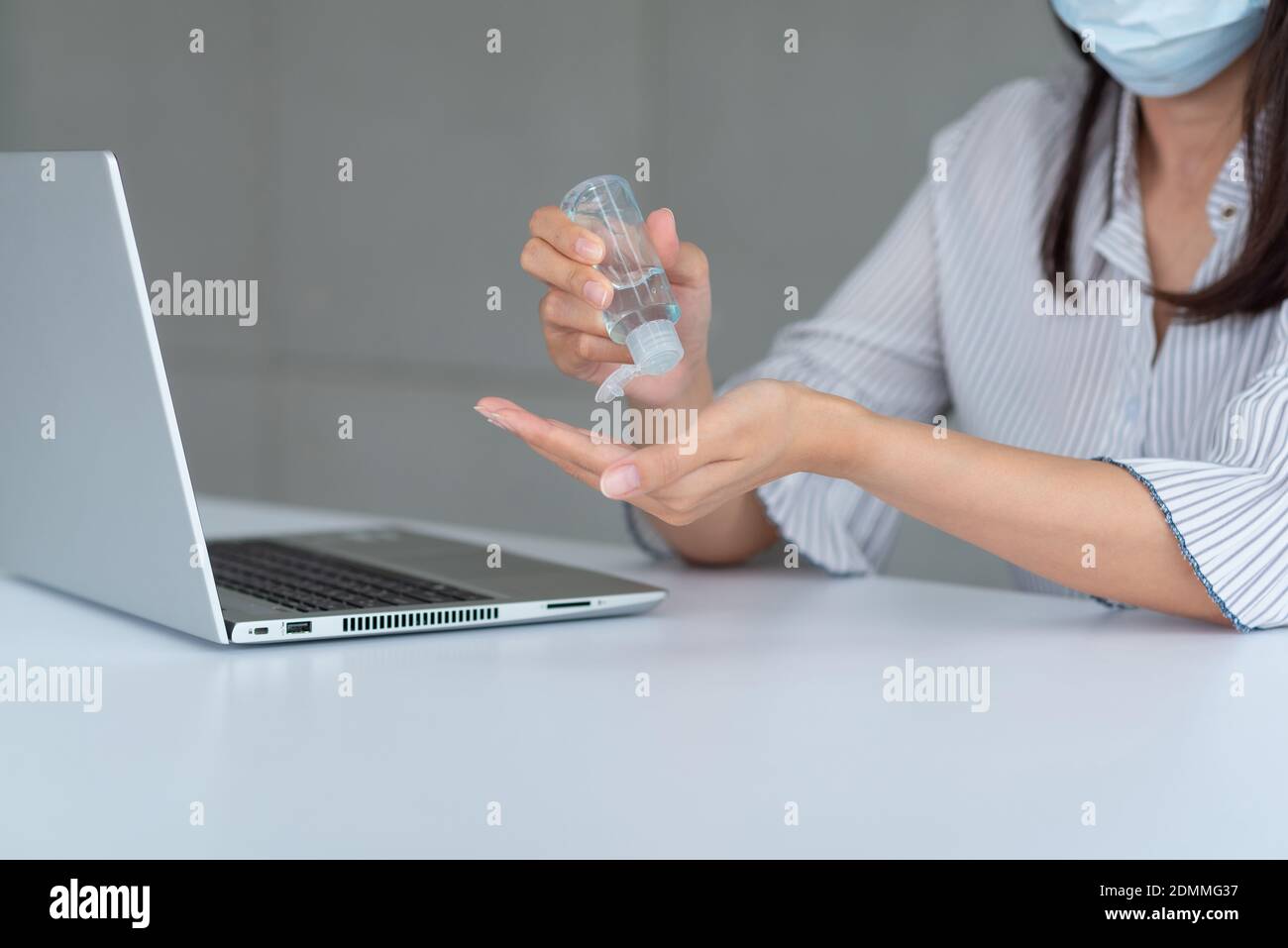 Donna d'affari che indossa la maschera e usa l'igienizzatore personale per la pulizia La sua mano in ufficio per mantenere l'igiene.preventiva durante il periodo di epidemia da Foto Stock