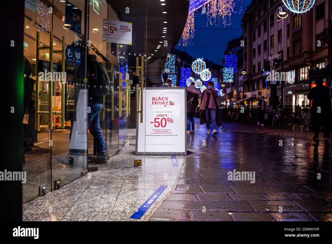 Strasburgo, Francia - 4 dicembre 2020: Folla di persone che entrano nel grande centro commerciale di lusso di notte con iscrizione sul banner d'ingresso - venerdì nero fino al 50% di sconto - natale decorato strada in background Foto Stock