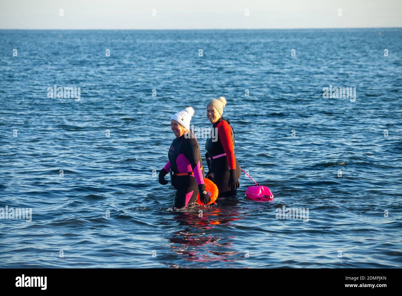 Due persone che entrano nel Mare del Nord circa per andare a nuotare, indossando mute, Kirkcaldy , Fife, Scozia Foto Stock