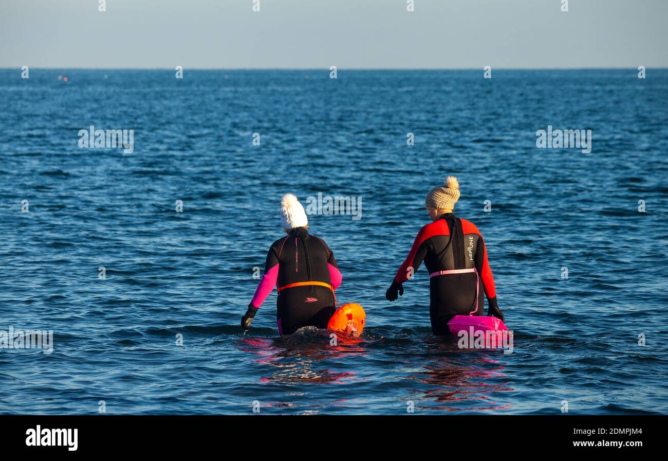 Due persone che entrano nel Mare del Nord circa per andare a nuotare, indossando mute, Kirkcaldy , Fife, Scozia Foto Stock