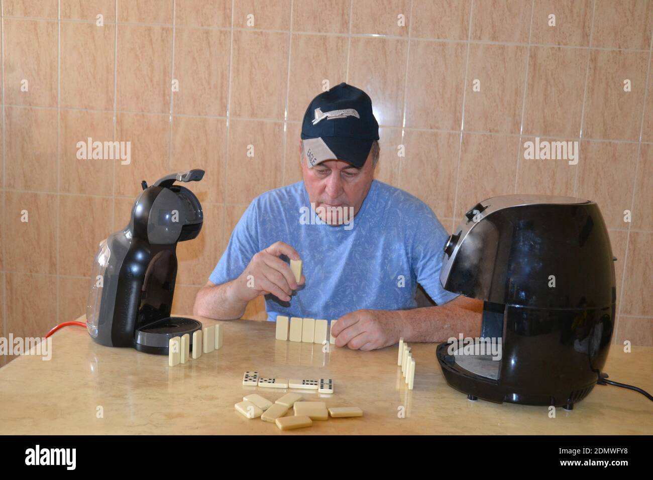 Uomo anziano che gioca a domino con i suoi nuovi amici in quarantena su un tavolo di marmo Foto Stock
