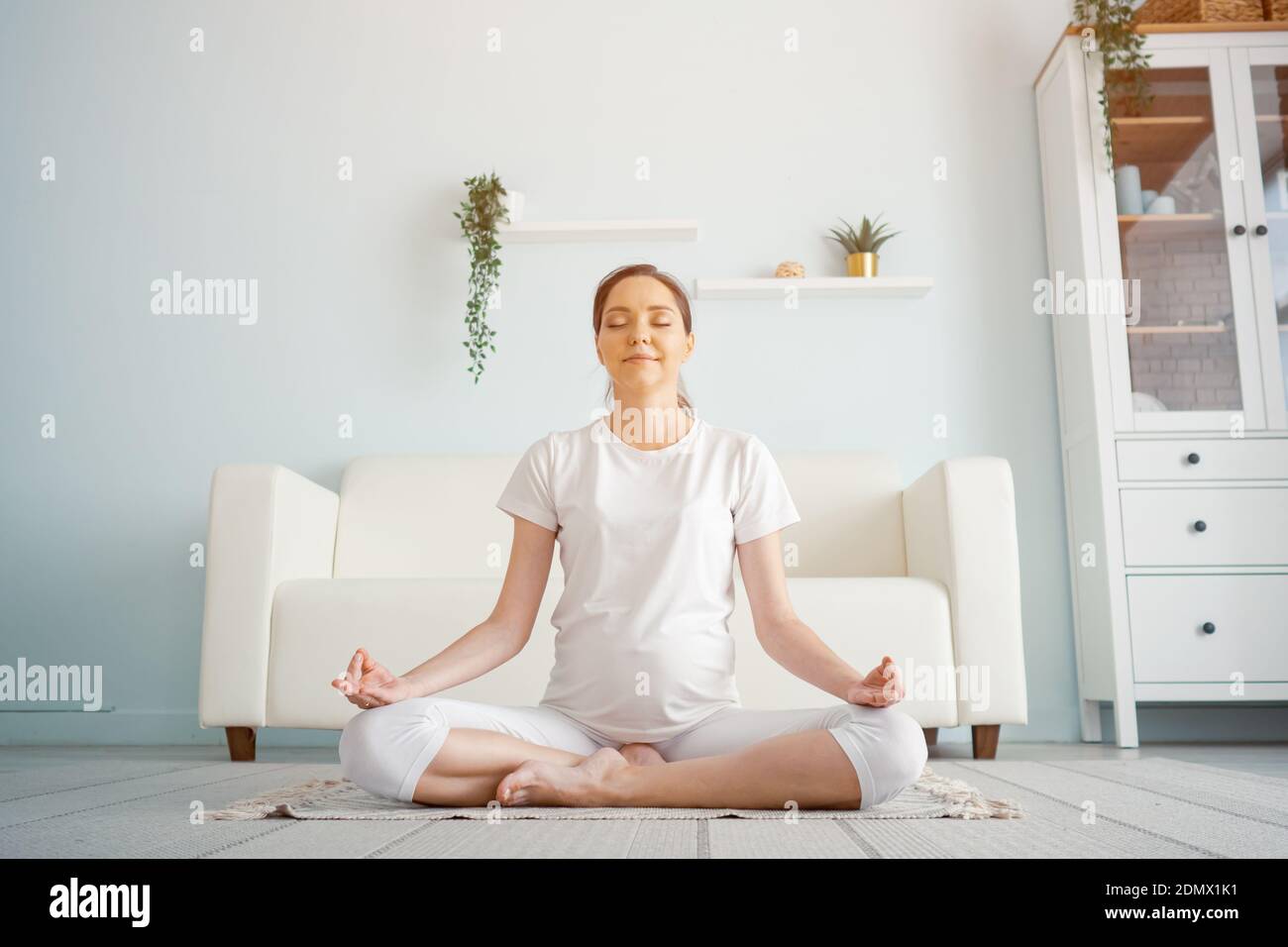 donna incinta sorridente in postura di loto che pratica luce solare yoga Foto Stock