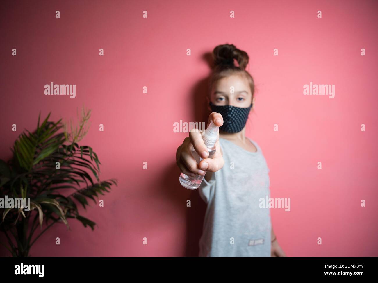 Una ragazza adolescente in una maschera medica tiene un antisettico nelle sue mani. Il concetto di lotta contro la COVID-19 Foto Stock