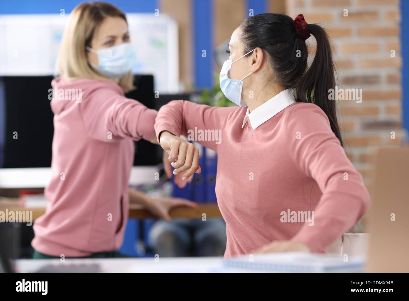 Due donne in ufficio in maschere mediche protettive salutano in modo sicuro Foto Stock