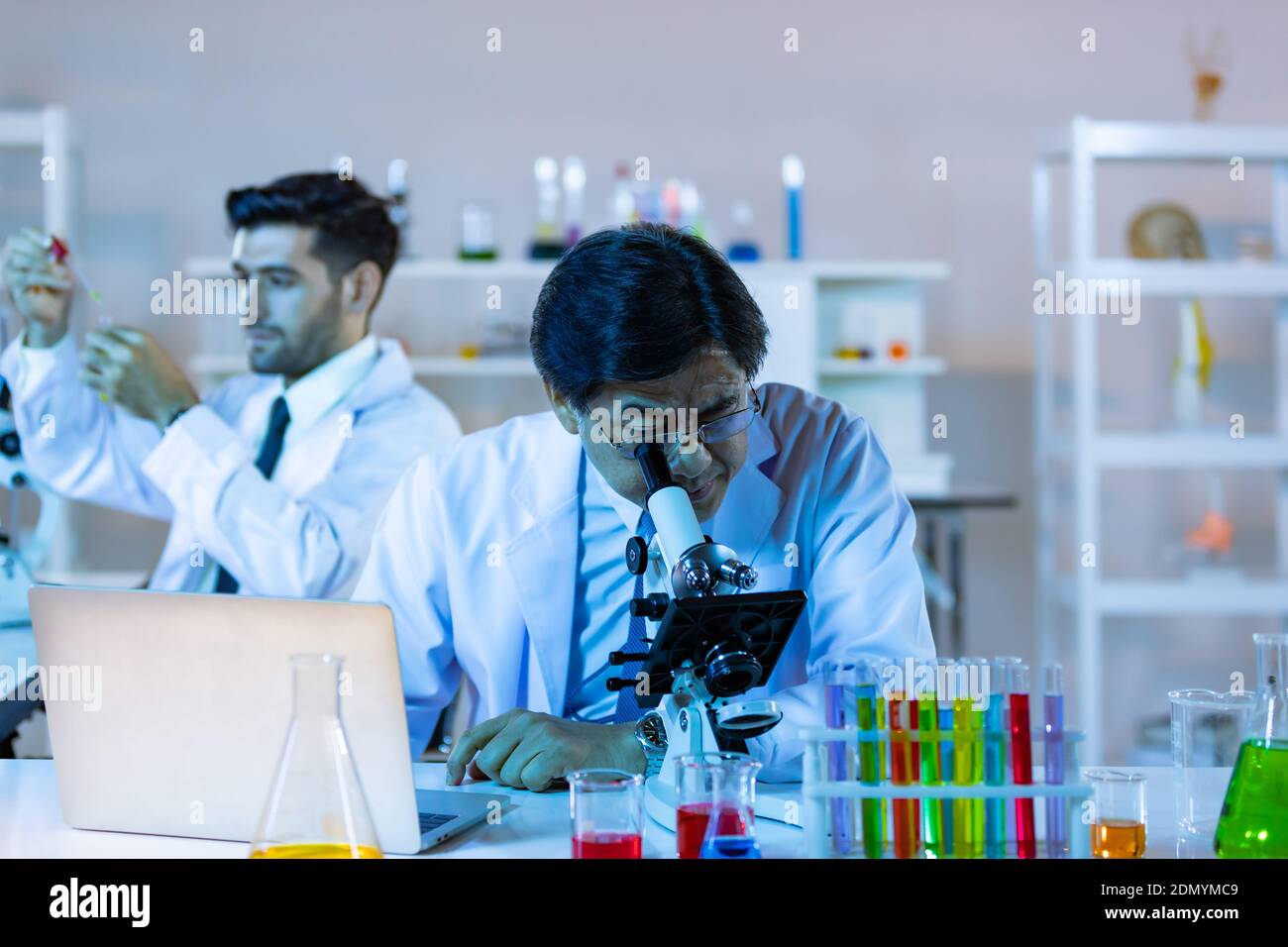 Il ricercatore di biotecnologia microbiologa o il team di lavoratori medici osservano il microscopio in laboratorio per la ricerca di dati chimici da parte di scienziati asiatici. Foto Stock