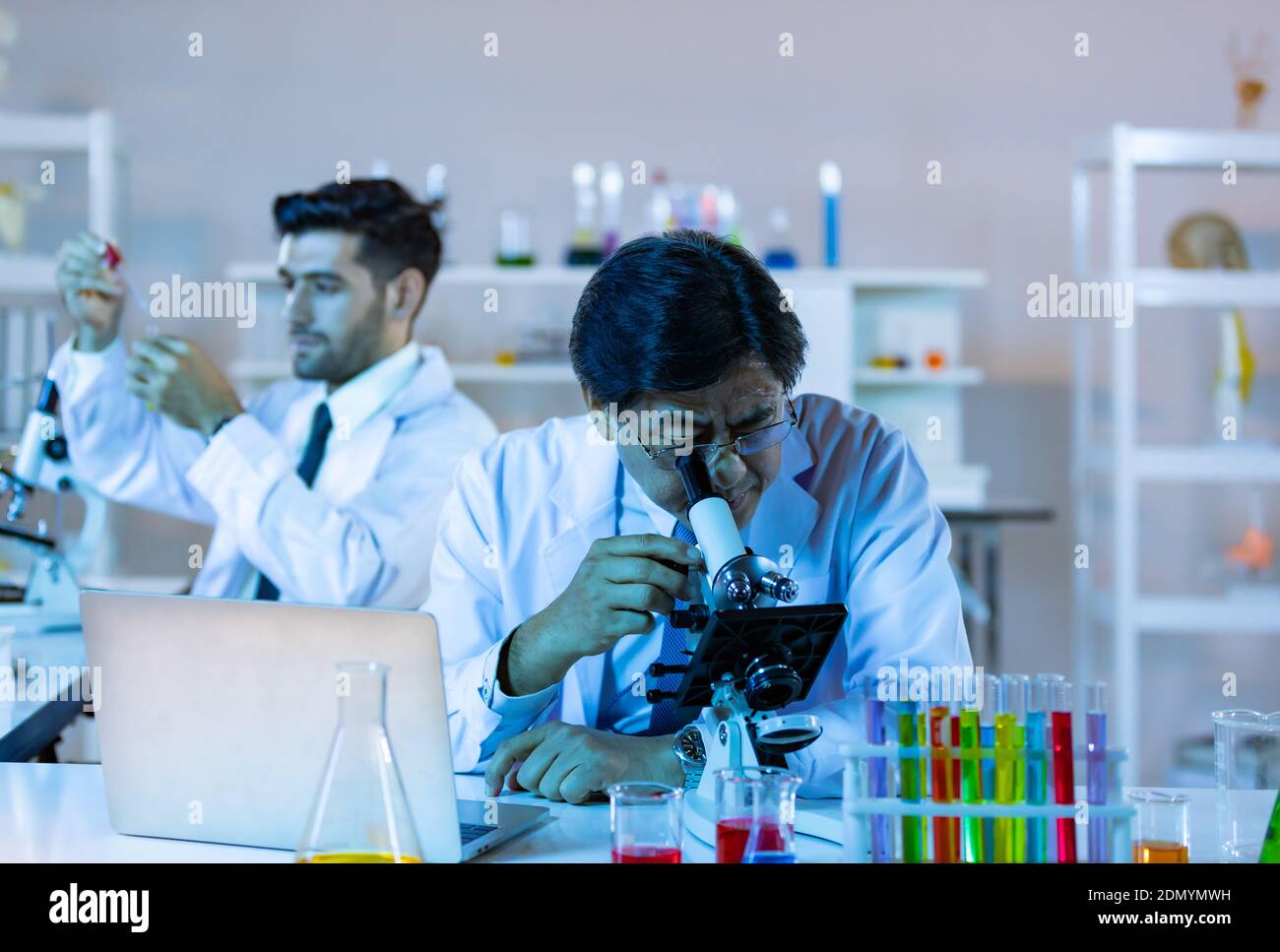 Il ricercatore di biotecnologia microbiologa o il team di lavoratori medici osservano il microscopio in laboratorio per la ricerca di dati chimici da parte di scienziati asiatici. Foto Stock