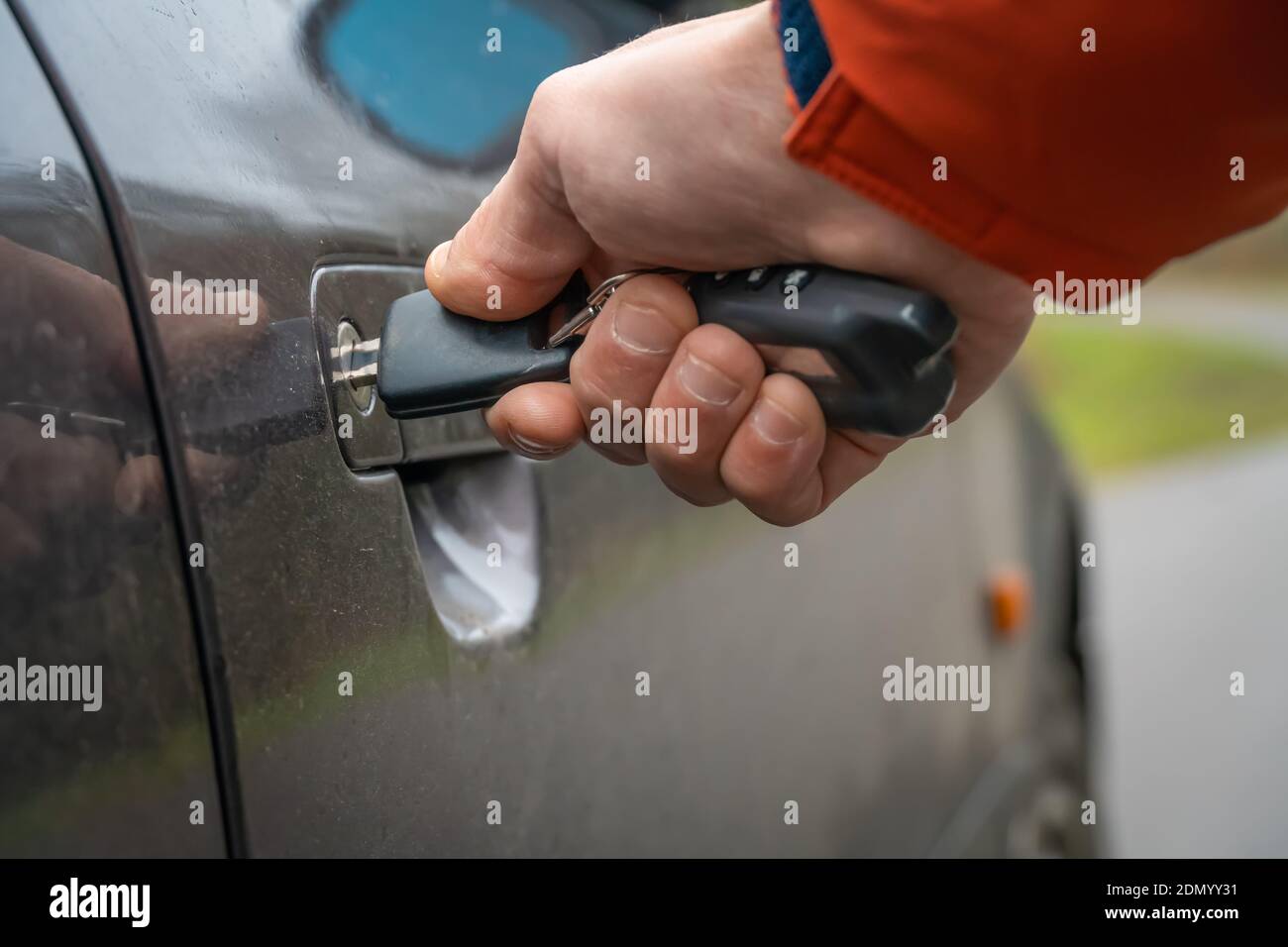 Primo piano della mano destra di un uomo in una giacca arancione inserendo una chiave nella serratura della porta dell'auto. Foto Stock