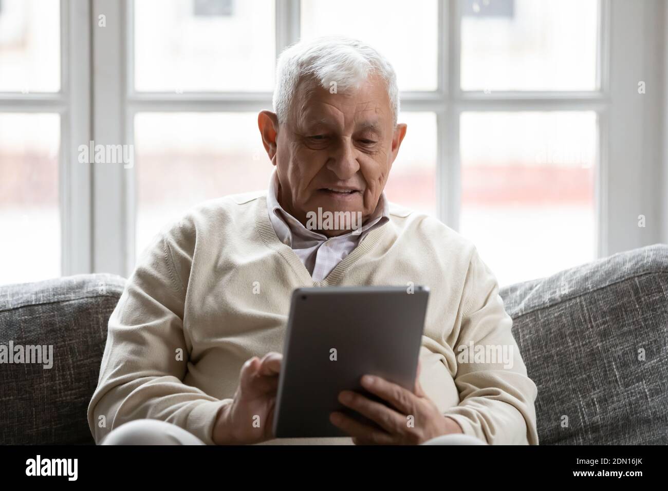 Uomo pensionato positivo che si rilassa sul comodo divano utilizzando un computer tablet Foto Stock
