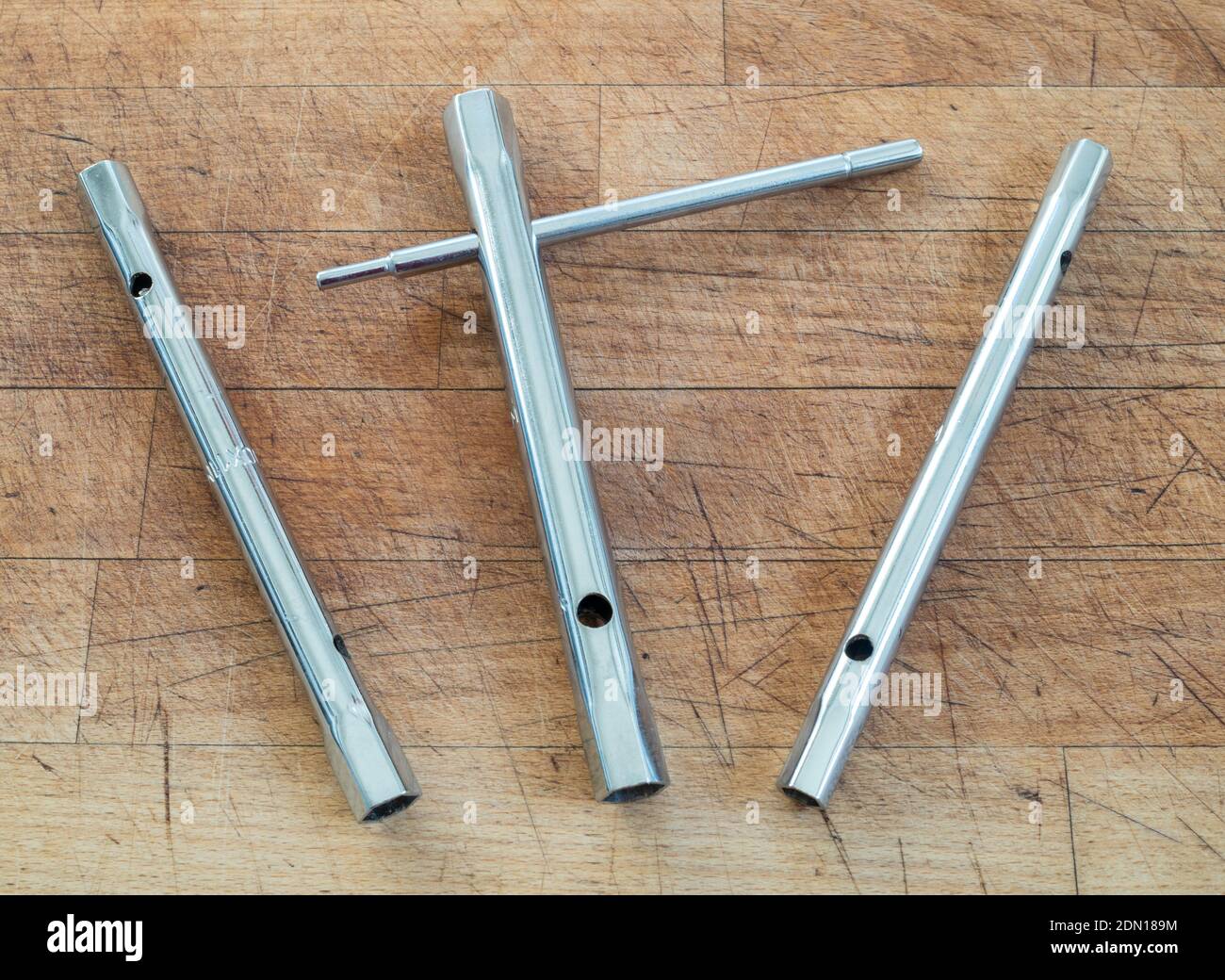 Un set di tre chiavi metriche tubolari o a tubo con una barra scorrevole o tommy su un fondo di legno. Foto Stock
