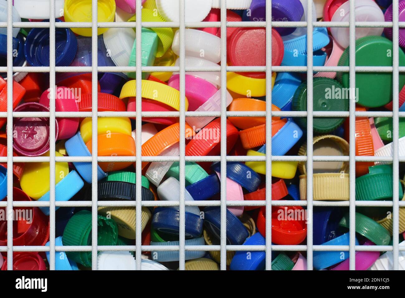Raccolta di tappi per bottiglie in plastica colorata in un contenitore metallico a griglia per il riciclaggio Foto Stock