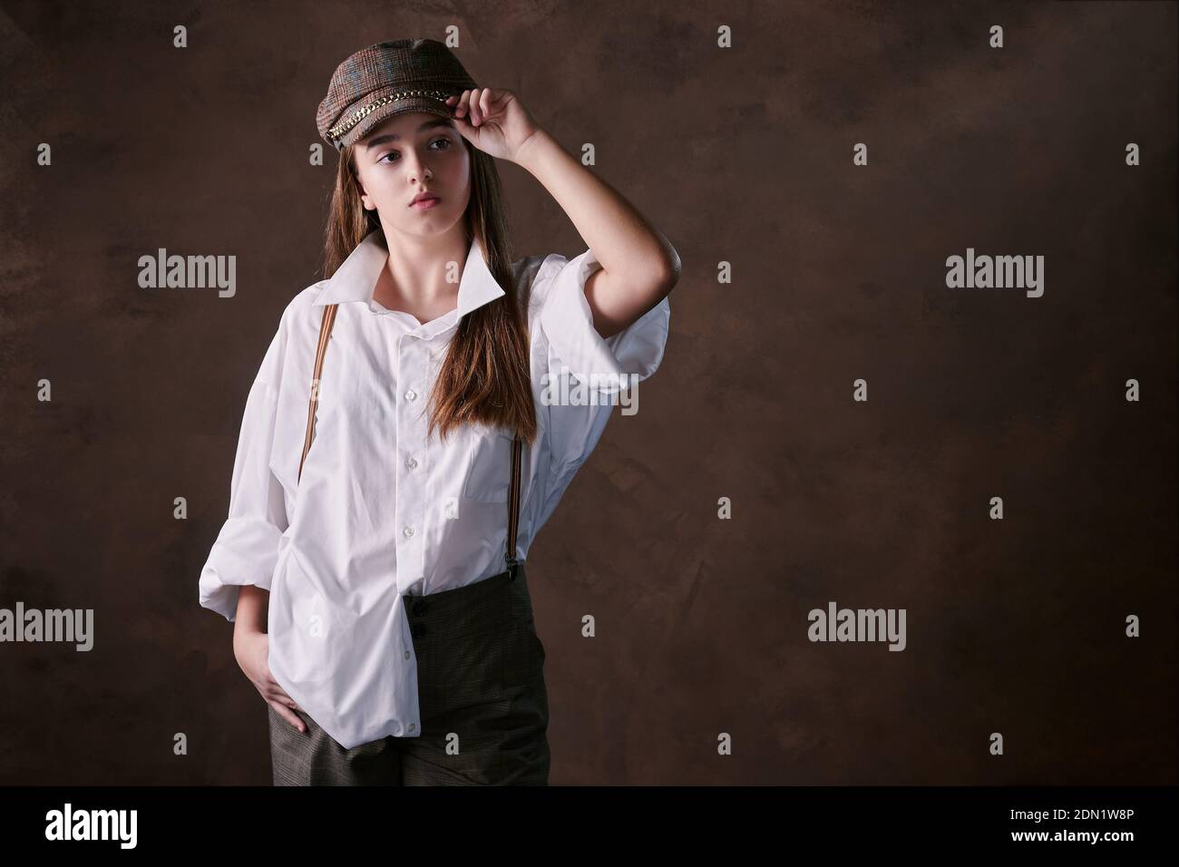 ragazza adolescente in un cappello con visiera in una camicia bianca e  pantaloni. studio sfondo marrone, moda Foto stock - Alamy