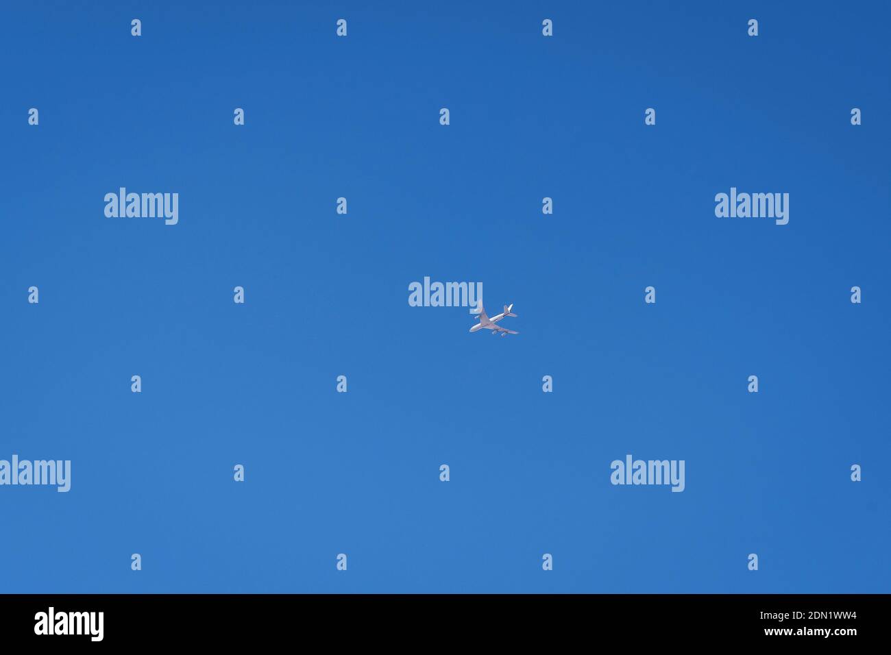 un drone bianco luminoso che assomiglia ad un aereo normale fotografato da terra che vola attraverso una grande area di cielo blu chiaro Foto Stock