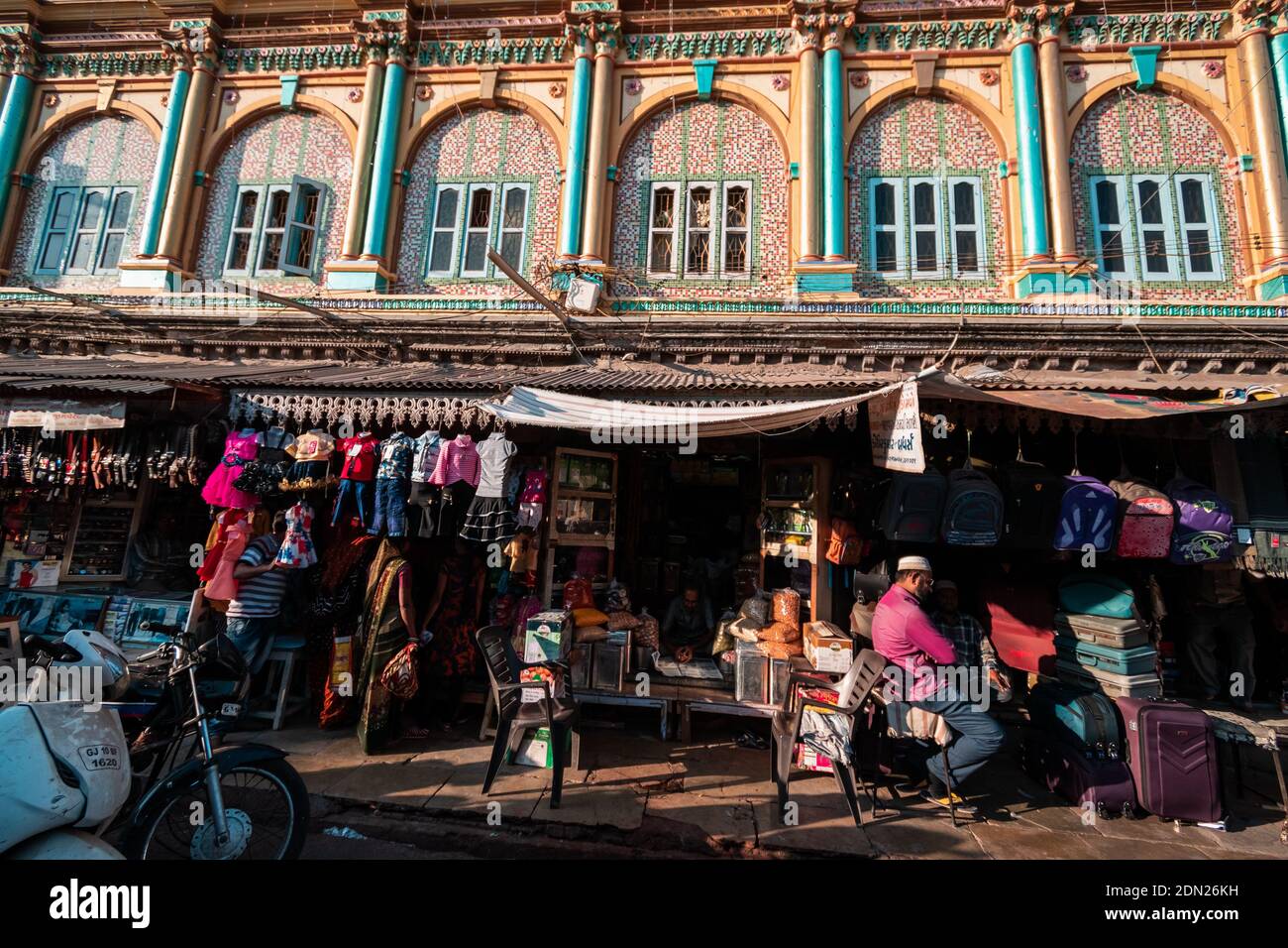 Jamnagar, Gujarat, India - Dicembre 2018: Un mercato affollato e negozi sotto le pareti ornate e le finestre ad arco dell'antica Jama masjid nel vecchio c. Foto Stock