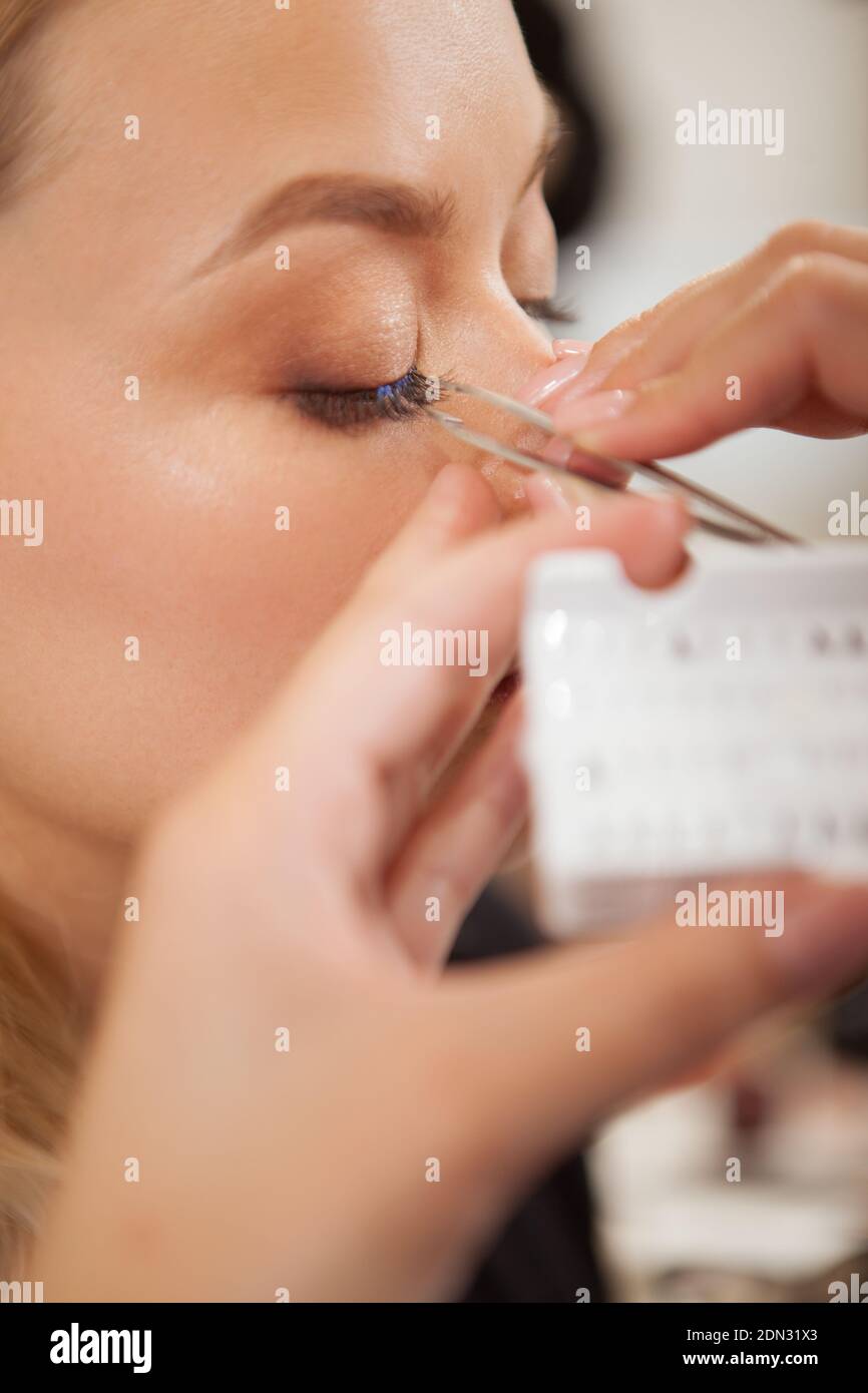 Primo piano verticale di una donna che ottiene le ciglia false applicate da professionista trucco artista Foto Stock