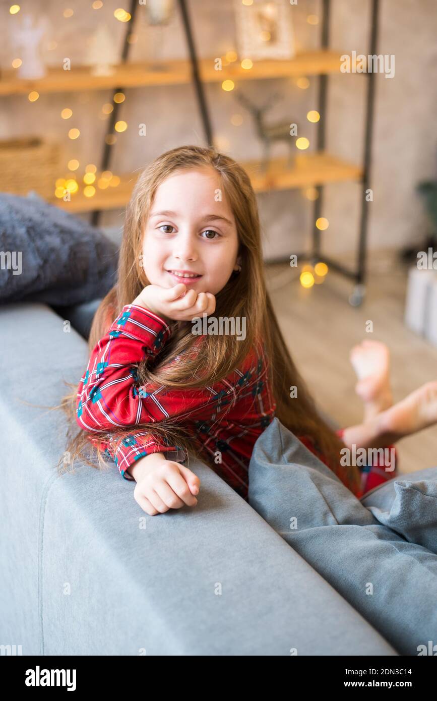 Felice bambina in pajama seduta su un divano grigio in soggiorno moderno Foto Stock
