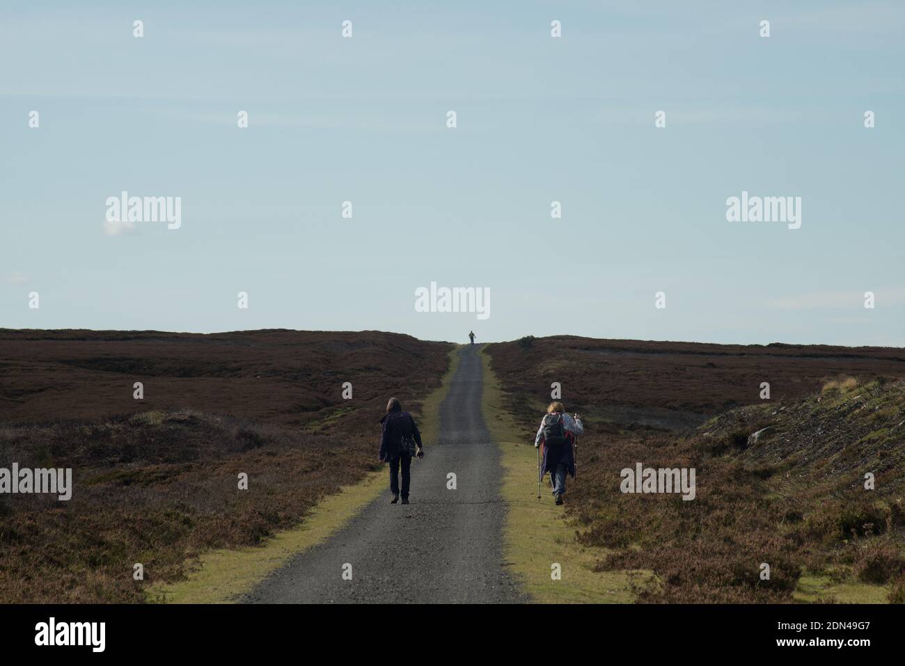 Due donne camminatrici che si dirigono lungo il sentiero della brughiera di Waskerly Way con un singolo camminatore delineato sull'orizzonte lontano che forma una forte forma triangolare Foto Stock